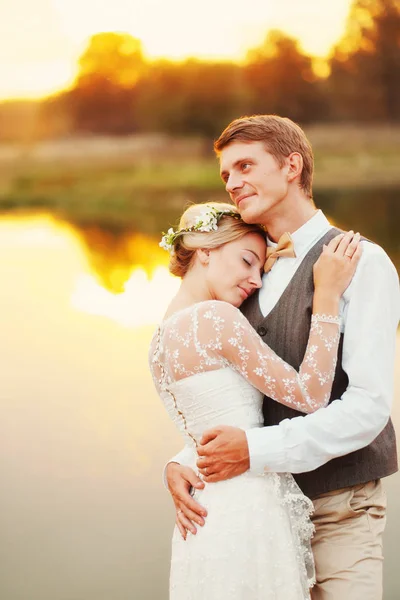 Noiva feliz e noivo abraçando contra o pano de fundo do lago — Fotografia de Stock