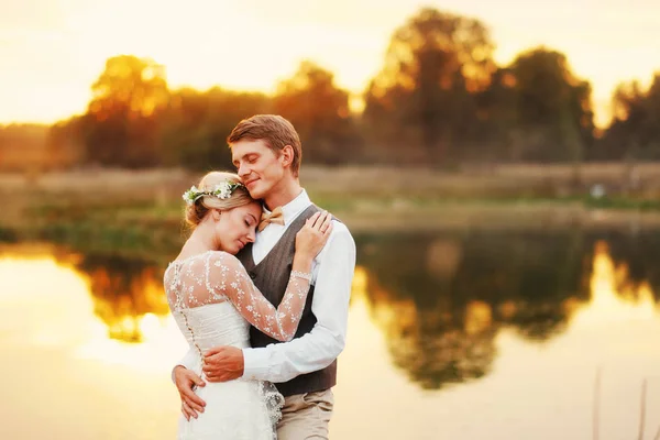 Portret van een bruidspaar tegen de achtergrond van het water bij zonsondergang zon. Op de achtergrond een lake — Stockfoto