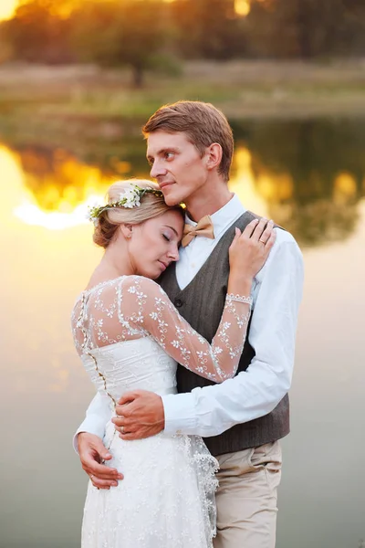 Os recém-casados ficam em frente a um lago ao pôr-do-sol — Fotografia de Stock