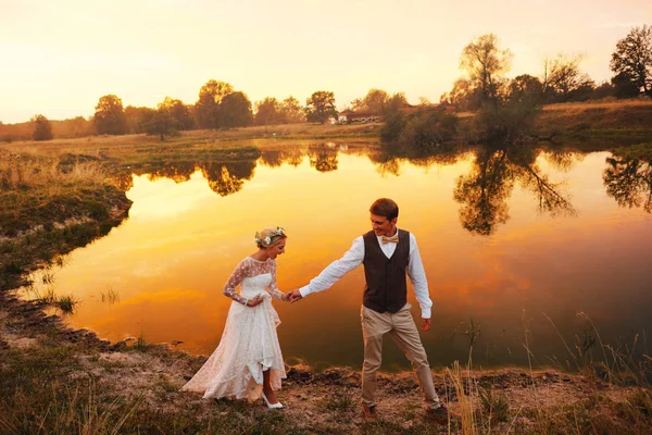 Gelin ve damat göl arka planı kırmızı günbatımı yürümek. Genel planı