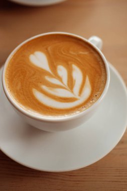 Güzel kokulu kapuçino stand ahşap bir masa üzerinde beyaz fincan. Masada, önden görünüm sütlü kahve.