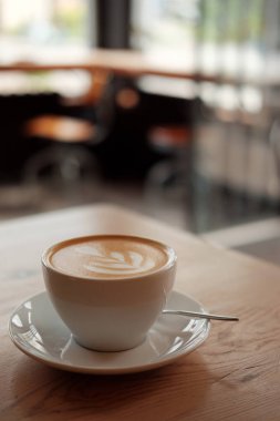 Güzel kokulu kapuçino stand ahşap bir masa üzerinde beyaz fincan. Masada, önden görünüm sütlü kahve.