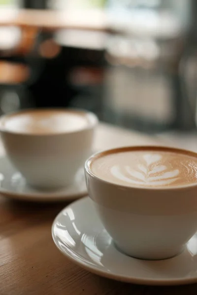 Deux tasses blanches de cappuccino parfumé se tiennent sur une table en bois. Café avec du lait sur la table, vue de face . — Photo