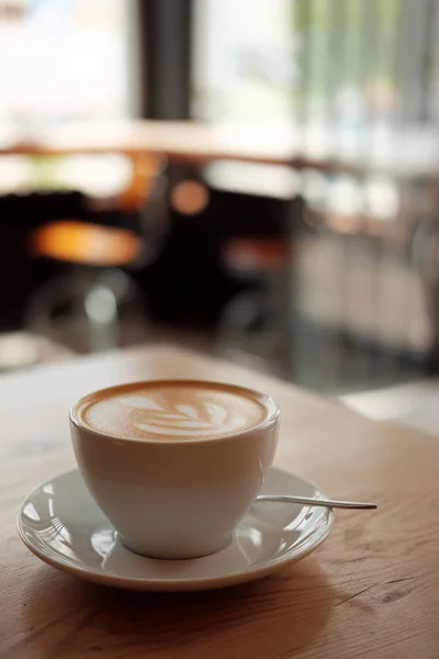 Güzel kokulu kapuçino stand ahşap bir masa üzerinde beyaz fincan. Masada, önden görünüm sütlü kahve. — Stok fotoğraf