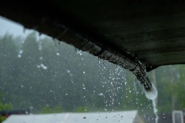 Hay un aguacero. Desde el techo de la casa de campo fluye agua. fuerte lluvia . — Foto de Stock