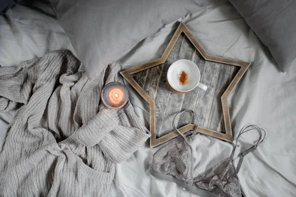 A cup of coffee and a candle in a Scandinavian wooden tray in a cozy bed with pillows. — Stock Photo, Image