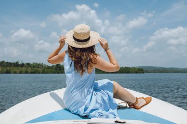 Şapkalı bir genç kadın yelkenli cephede oturur ve görünümü hayran