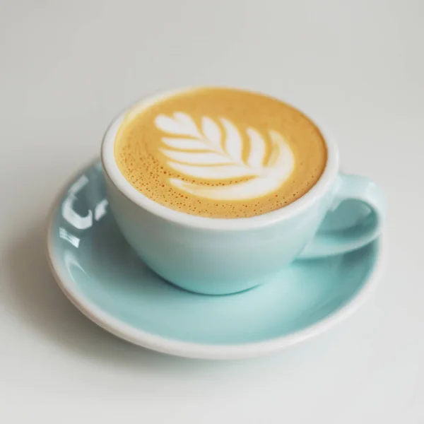 En kopp kaffe i en vacker blå kopp på bord på caféet. En cappuccino mugg med mönster på skummet. — Stockfoto