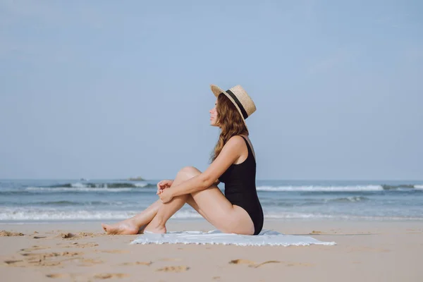 Meisje in een stro hoed zittend op het strand in de buurt van de Oceaan — Stockfoto