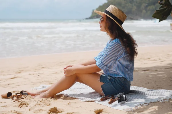 Meisje in een hoed zit op het strand en de Oceaan kijkt — Stockfoto
