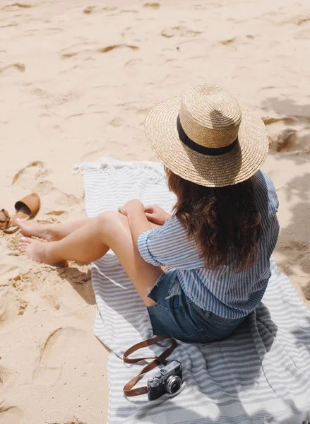 Girl in a hat on the beach sits on the sand under a tree