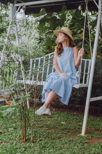 Mujer joven en un sombrero se sienta en un columpio blanco — Foto de Stock