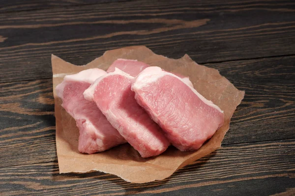 Bistecche fresche di maiale crudo su carta su fondo di legno scuro . — Foto Stock