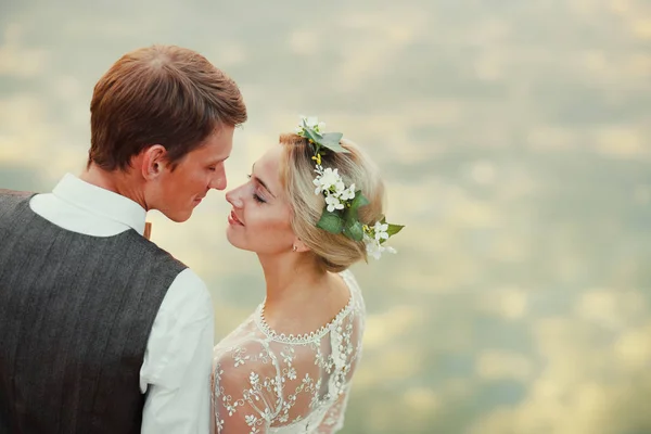 Bruden och brudgummen står vid sjön efter vigseln. Nygifta leende, de är glada. Foto i varm toning. Närbild. — Stockfoto