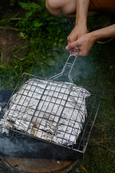 Homme faire frire du poisson dans une feuille sur un gril — Photo