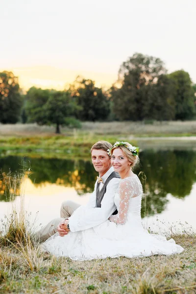 Pareja feliz en traje de boda en el fondo del lago al atardecer, la novia y el novio en un vestido blanco . — Foto de Stock