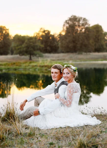 Casal em traje de casamento contra o pano de fundo do lago ao pôr do sol, a noiva eo noivo . — Fotografia de Stock