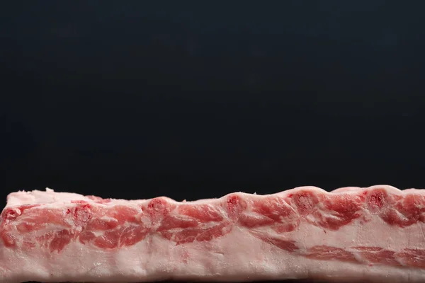 Cremalheira inteira crua fresca de lombo de porco com costelas em um fundo escuro. Vista frontal — Fotografia de Stock