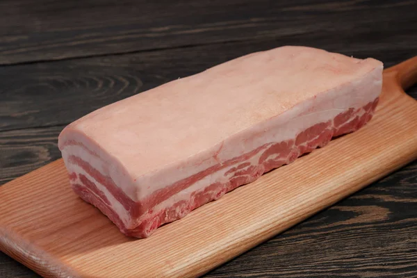 Fresh raw whole rack of pork loin with ribs and fat on a cutting board on a dark background. — Stock Photo, Image