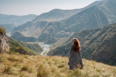 Uzun elbiseli güzel genç kadın dağ vadisinde duruyor
