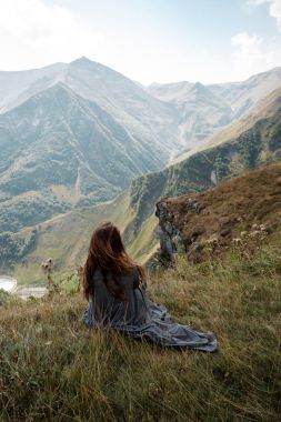 Uzun elbiseli güzel genç kadın uçurumdan Dağları arka planda oturuyor