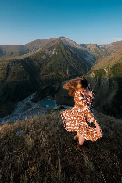 Hermosa joven con un vestido largo está de pie en un acantilado de una montaña . — Foto de Stock