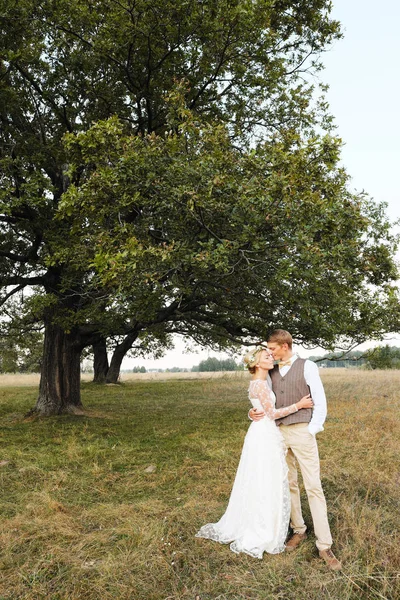 La novia y el novio están en el fondo del árbol, después de la ceremonia de la boda. Los recién casados sonríen, son felices. . — Foto de Stock