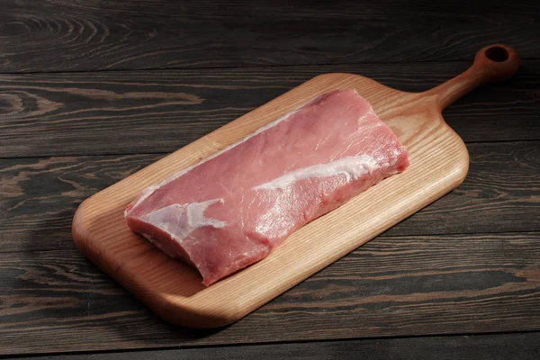 Whole boneless pork loin without fat. Pork tenderloin on a cutting board on a dark background