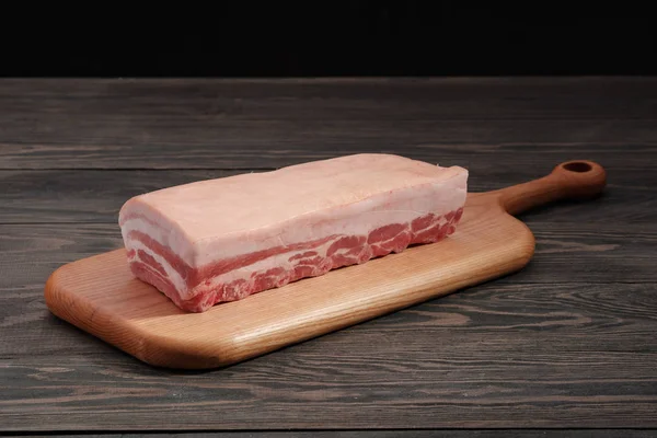 Carré di maiale crudo fresco intero con costole e grasso su un tagliere su sfondo scuro . — Foto Stock