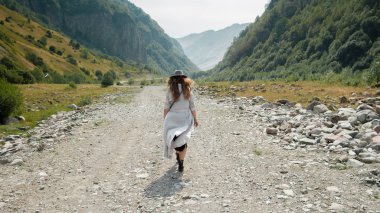 Dağlara doğru yolun ortasında boyunca şapkalı bir kız yürüyor 