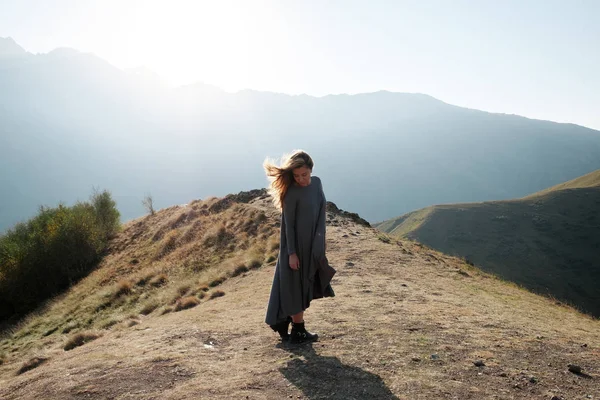 Una hermosa chica en un vestido volador está de pie en un acantilado con vistas a las montañas — Foto de Stock