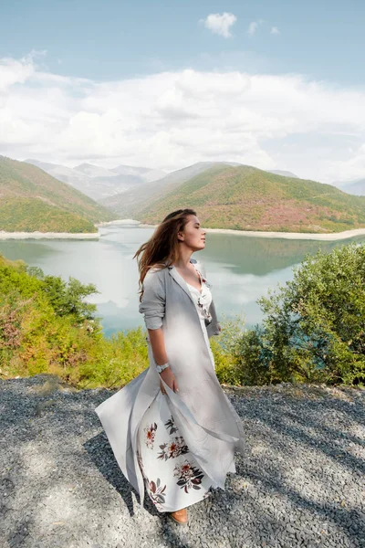 Hermosa chica en un vestido largo sobre un fondo de un lago y montañas — Foto de Stock