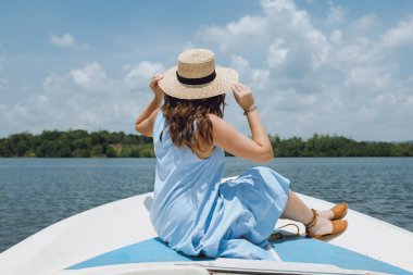 Şapkalı bir genç kadın yelkenli cephede oturur ve görünümü hayran