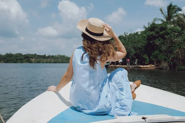 Achteraanzicht van een jonge vrouw in een stro hoed ontspannen op een boot en kijken naar de rivier — Stockfoto