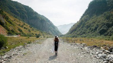 Bir kız bir şapka ve bot, yolun karşı zemin Dağları nın ortasında yürüyor