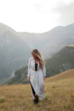 Uzun elbiseli güzel genç kadın dağ vadisinde duruyor