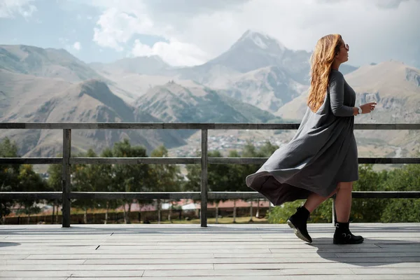Una chica está caminando con una copa de vino en la terraza con vistas a las montañas — Foto de Stock