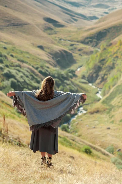 Una hermosa chica en un vestido volador está de pie junto a un acantilado en las montañas — Foto de Stock