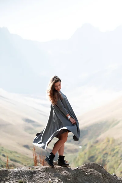 Joven hermosa chica en un vestido largo está de pie junto al acantilado en el fondo de las montañas — Foto de Stock