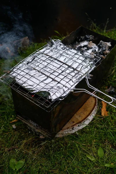 La parrilla con pescado en papel de aluminio se encuentra en la parrilla —  Fotos de Stock