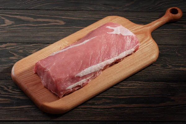 Lombata intera di maiale disossata senza grasso. Filetto di maiale su un tagliere su sfondo scuro — Foto Stock