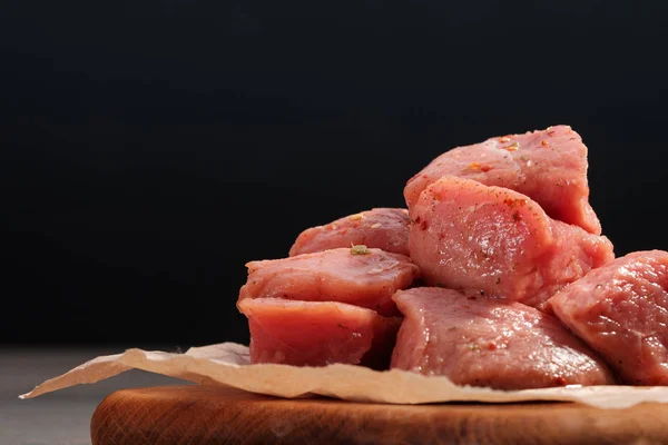 Brocheta de cerdo picante cruda en papel sobre una tabla de cortar sobre un fondo oscuro — Foto de Stock
