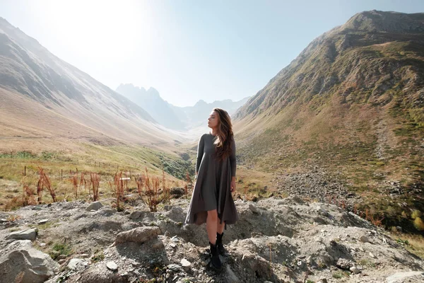 Hermosa joven con un vestido largo está de pie en el valle de las montañas — Foto de Stock