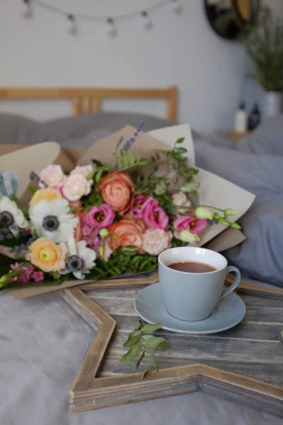 Buquê de flores e uma xícara de chá na cama — Fotografia de Stock