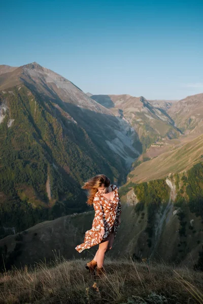 Hermosa joven con un vestido largo está de pie en un acantilado de una montaña . — Foto de Stock