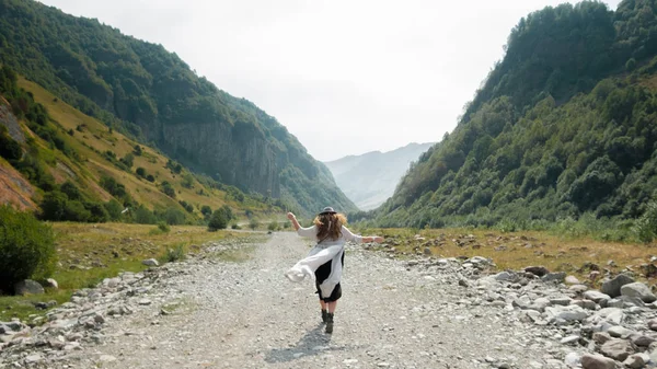 Una chica con sombrero camina por el medio del camino hacia las montañas — Foto de Stock
