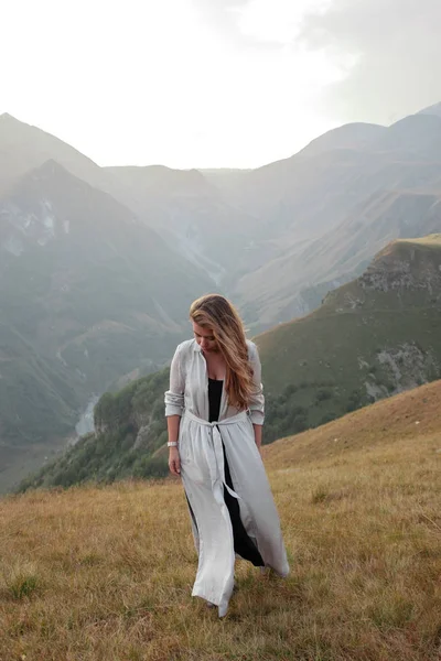 Hermosa joven con un vestido largo está de pie en el valle de las montañas — Foto de Stock