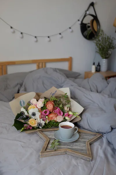 Μπουκέτο με λουλούδια και ένα φλιτζάνι τσάι στο κρεβάτι — Φωτογραφία Αρχείου