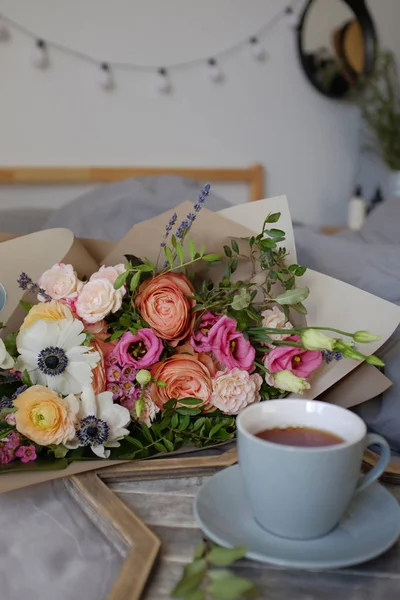 Bouquet of flowers and a cup of tea on the bed — Stock Photo, Image