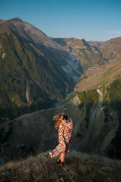 Hermosa joven con un vestido largo está de pie en un acantilado de una montaña . — Foto de Stock